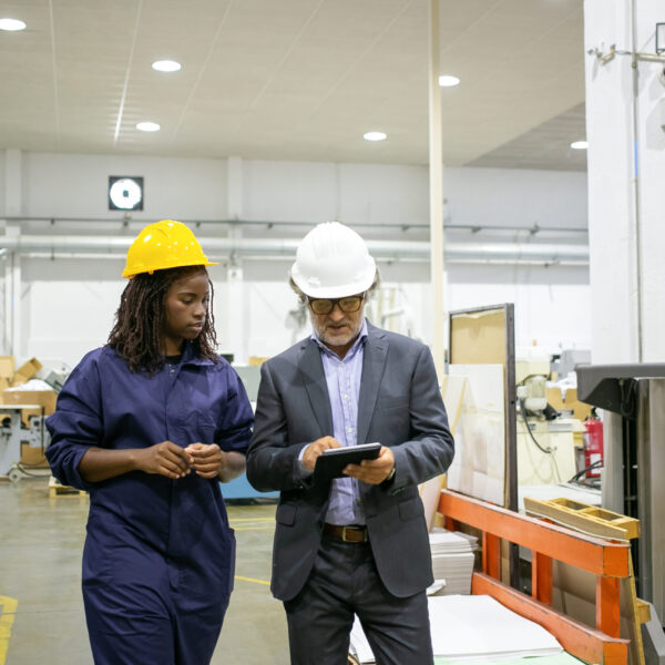 Caucasian manager discussing factory work with African worker Caucasian manager discussing factory work with African worker. Beautiful pensive young woman working on plant and looking on tablet in supervisor hands. Manufacture and digital technology concept